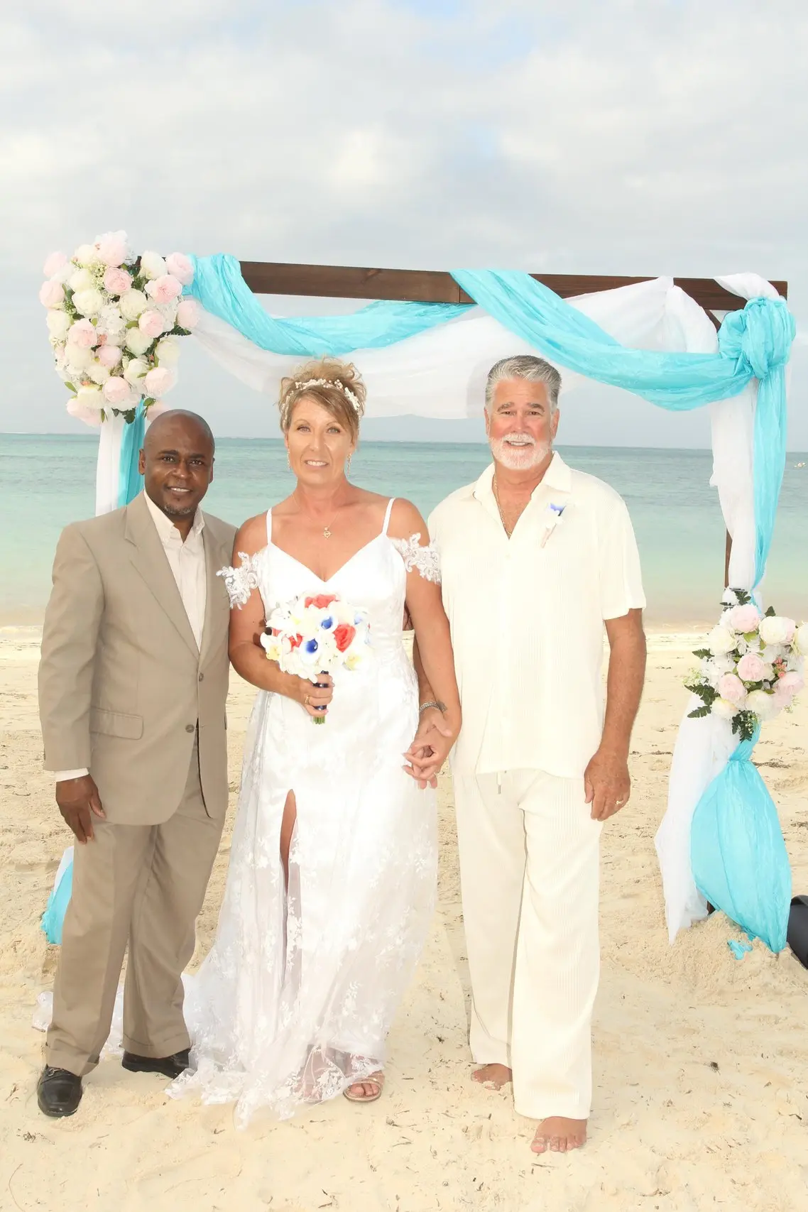 A couple with Antonio Beckford under a turquoise-draped ceremony arch.