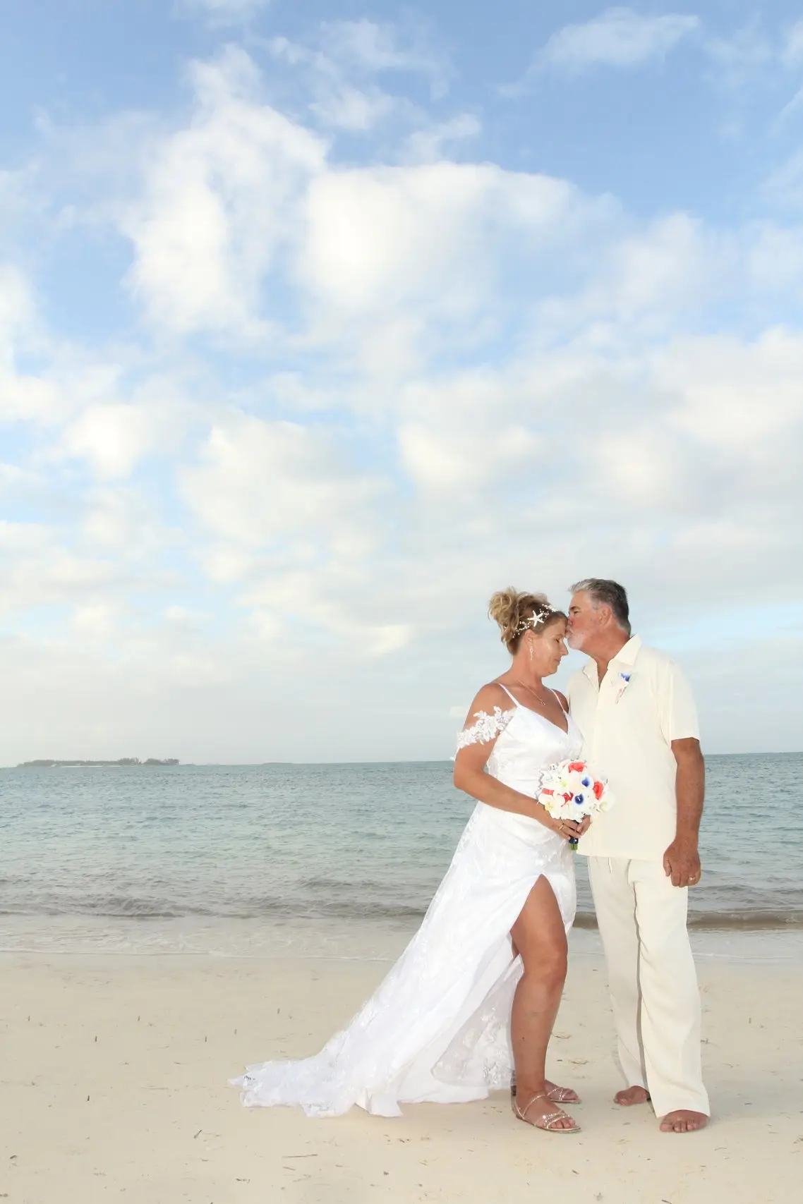 A couple kissing on the beach beneath an open sky.