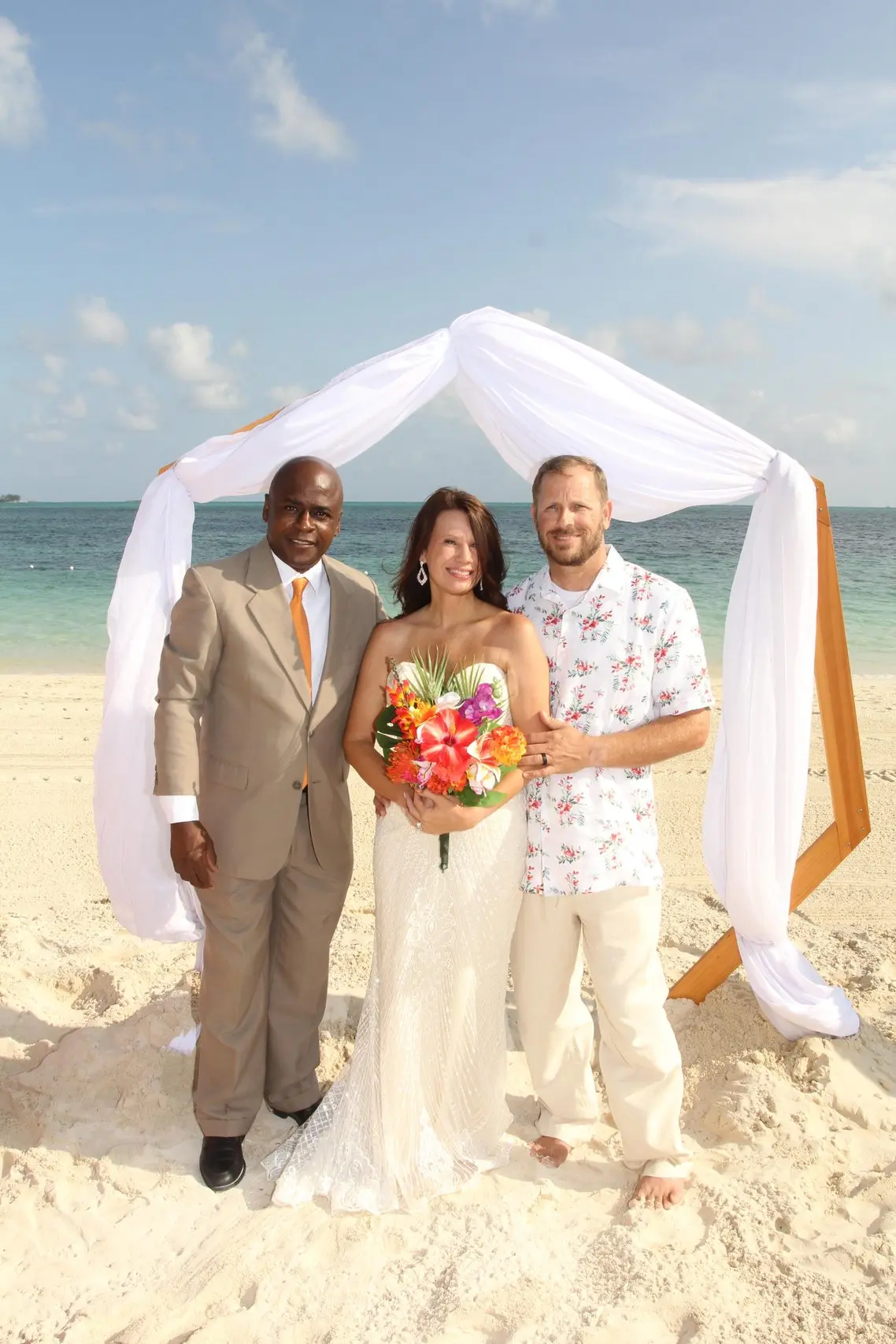 A couple with Antonio Beckford under a white draped ceremony arch.