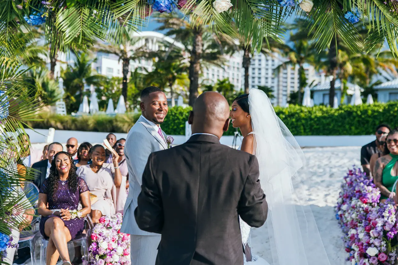 A beach ceremony with seated guests and a lit tiki torch.